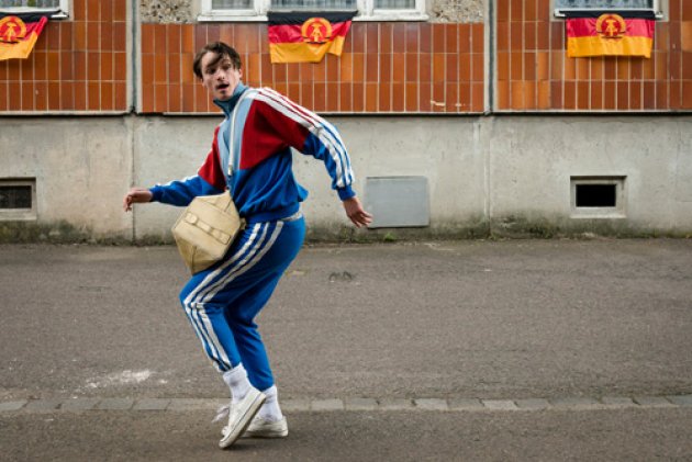 Mann, Breakdance, DDR, Häuserfront, weiße Schuhe, weiße Socken, Blauer Trainingsanzug, weiße Streifen, beige Tasche, Hellblau, rot, grau, Bürgersteig